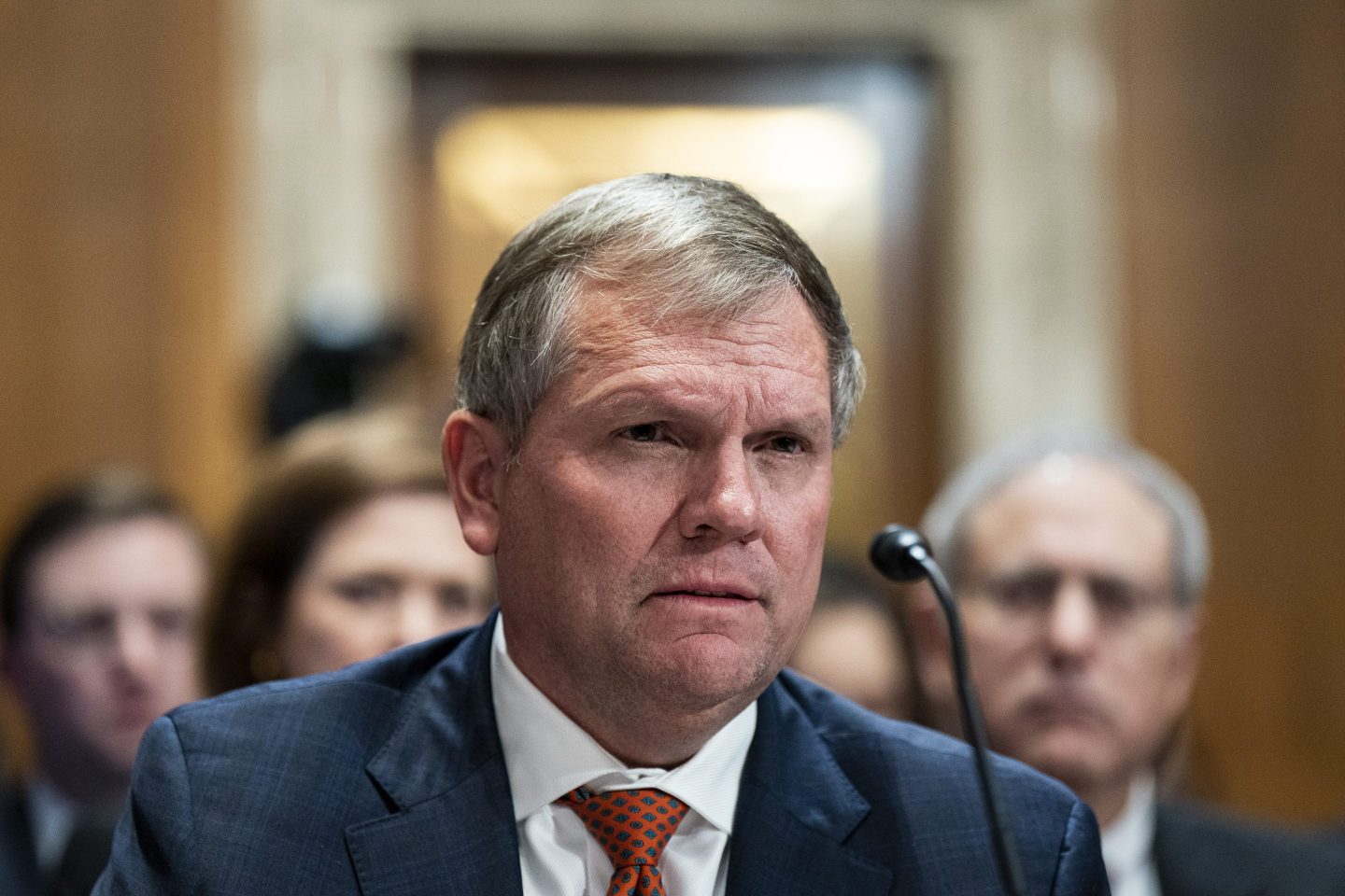 Alan Shaw, dressed in a blue suit and orange tie, looks intently in front of a microphone at a hearing on Capitol Hill.