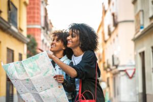 Afro Young Mother Using a Map with her Daughter . Mother and Daughter on Vacations or Holidays in Europe . Afro American Sisters Looking an Address in the Street. Holidays Concept.