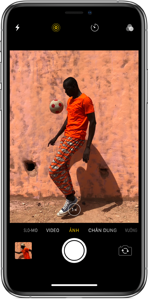 Màn hình Camera ở chế độ Ảnh, với các chế độ khác ở bên trái và phải bên dưới trình xem. Các nút cho Flash, Live Photo, Hẹn giờ và Bộ lọc xuất hiện ở đầu màn hình. Một hình ảnh thu nhỏ có thể chạm được ở phía dưới bên trái cung cấp quyền truy cập để xem các ảnh và video hiện có. Nút Chụp ảnh ở phía dưới cùng ở giữa và nút Chuyển camera ở phía dưới bên phải.