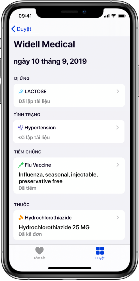 Tiêu đề “Widell Medical” xuất hiện gần đầu màn hình trong ứng dụng Sức khỏe. Bên dưới tiêu đề, thông tin về một số loại hồ sơ sức khỏe xuất hiện. Danh mục trên cùng, Dị ứng, chứa một hồ sơ, Lactose (Đã ghi hồ sơ). Một điều khiển mũi tên ở bên phải cho biết có các thông tin khác dành cho hồ sơ. Màn hình bao gồm hồ sơ sức khỏe bổ sung cho các danh mục Tình trạng, Tiêm chủng và Thuốc.