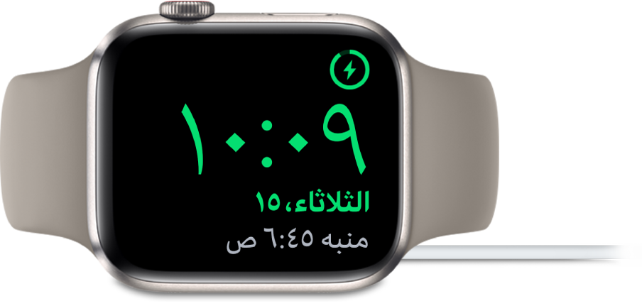Apple Watch موضوعة على جانبها ومتصلة بالشاحن، وتعرض الشاشة رمز الشحن في الزاوية العلوية اليمنى، والوقت الحالي أسفل ذلك، ووقت المنبه التالي.
