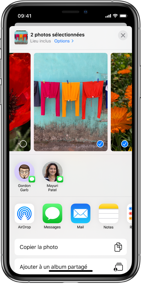 L’écran Partage avec des photos affichées en haut ; deux d’entre elles sont sélectionnées, comme indiqué par la coche blanche dans un rond bleu. Le rang sous les photos présente les amis avec lesquels vous pouvez les partager à l’aide d’AirDrop. D’autres options de partage sont proposées en dessous, notamment, de gauche à droite : Messages, Mail, Albums partagés et Ajouter à Notes. Le rang du bas contient les boutons suivants : Copier, Copier le lien iCloud, Diaporama, AirPlay, et Ajouter à un album.