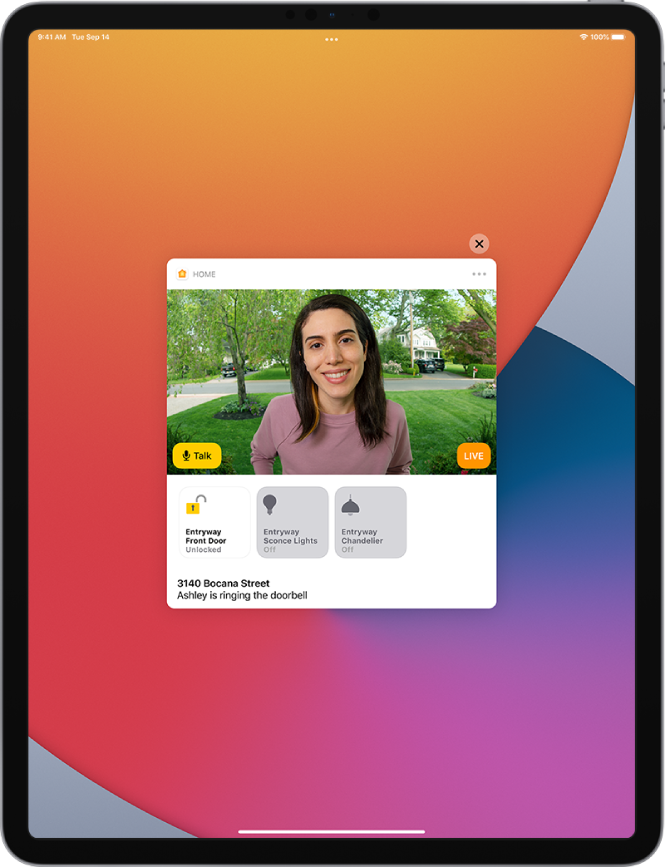 Известие от Home (Дом) на екрана на iPad. Показва снимката на човек на входната врата с бутона Talk (Говори) вляво. Отдолу са бутоните на аксесоарите за входната врата и за осветлението в коридора. В долния край е адресът на дома заедно с думите „Ashley is ringing the doorbell“ („Ашли звъни на звънеца“). В горния десен край на известието е бутонът Close (Затвори).