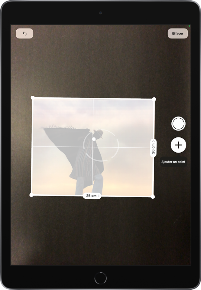 Une photographie papier est mesurée et ses dimensions s’affichent le long de ses bords droit et inférieur. Le bouton Prendre une photo est situé vers le milieu du bord droit. L’indicateur vert « Caméra en cours d’utilisation » apparaît en haut à droite.