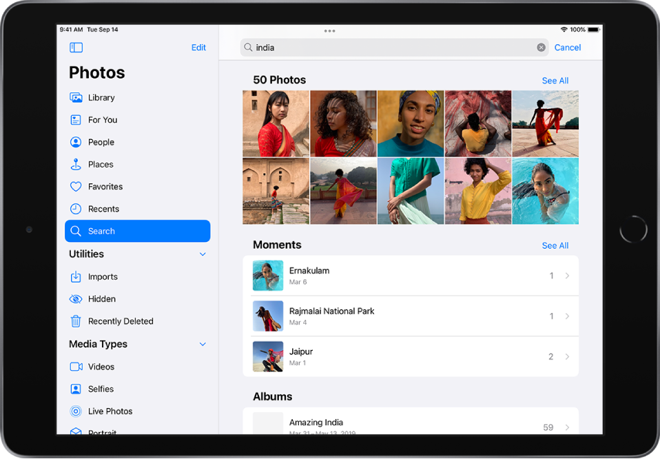 Lietotne Photos ir atvērta ainavorientācijā. Ekrāna kreisajā malā sānu joslā ir redzamas pogas Photos, For You, Albums un Search; ir atlasīta poga Search. Ekrāna augšpusē ir meklēšanas lauks; meklēšanas laukā ir ievadīta atrašanās vieta un datumi. Zem meklēšanas lauka ir saraksts ar ieteiktajiem meklēšanas rezultātiem. Ekrāna vidū ir pēc meklēšanas nosacījumiem atrasto fotoattēlu režģis. Fotoattēlu režģa augšējā kreisajā stūrī ir redzams meklēšanas rezultātos atrasto fotoattēlu kopskaits. Fotoattēlu režģa augšējā labajā stūrī ir poga See All.