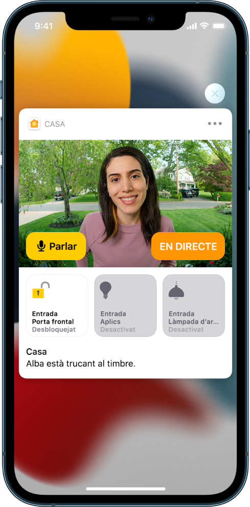 Notificació de l’app Casa a la pantalla de l’iPhone. Mostra la imatge d’una persona a la porta principal amb un botó per parlar a l’esquerra. A sota hi ha els botons dels accessoris per a la porta principal i els llums de l’accés d’entrada. Es mostren les paraules “La Laura està trucant al timbre”. A l’angle superior dret de la notificació hi ha un botó per tancar.