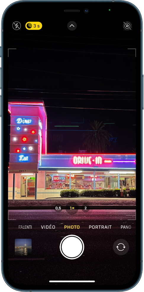 Écran de l’appareil photo en mode Photo. Les boutons correspondant au flash et au mode Nuit s’affichent dans l’angle supérieur gauche de l’écran. Le flash est désactivé et le mode Nuit est actif. Le bouton « Commandes de l’appareil photo » se trouve en haut au centre et le bouton « Live Photo » dans le coin supérieur droit. En bas de l’écran, de gauche à droite, se trouvent le bouton « Visualiseur de photos et vidéos », le bouton « Prendre une photo » et le bouton « Sélecteur de caméra - face arrière ».
