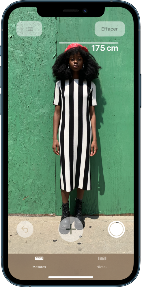 Une personne en train d’être mesurée, la taille s’affichant au-dessus de sa tête. Le bouton « Prendre une photo » est actif dans le coin inférieur droit, afin de prendre une photo de la mesure. L’indicateur vert « Caméra en cours d’utilisation » apparaît en haut à droite.