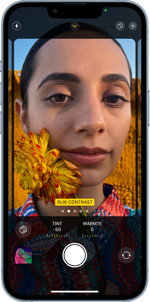 Camera is geopend en het scherm 'Fotografische stijlen' is te zien. Linksboven in het scherm staat de flitserknop. Middenboven in het scherm staat de knop voor cameraregelaars; deze is ingeschakeld. Rechtsbovenin staan de knoppen voor fotografische stijlen (ingeschakeld) en Live Photo. De stijl 'Rijk contrast' is in het opnamekader te zien en vult het camerascherm. Onder het opnamekader staan de knop voor stijlen, de schuifknoppen waarmee je de waarden voor tint en warmte aanpast en de knop voor het herstellen van de stijl. Onder in het scherm staan van links naar rechts de knop 'Foto- en videoweergave', de knop 'Maak foto' en de knop voor het kiezen van de camera aan de achterkant.