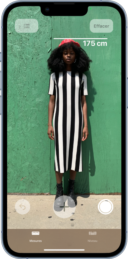 Une personne en train d’être mesurée, la taille s’affichant au-dessus de sa tête. Le bouton « Prendre une photo » est actif dans le coin inférieur droit, afin de prendre une photo de la mesure. L’indicateur vert « Caméra en cours d’utilisation » apparaît en haut à droite.