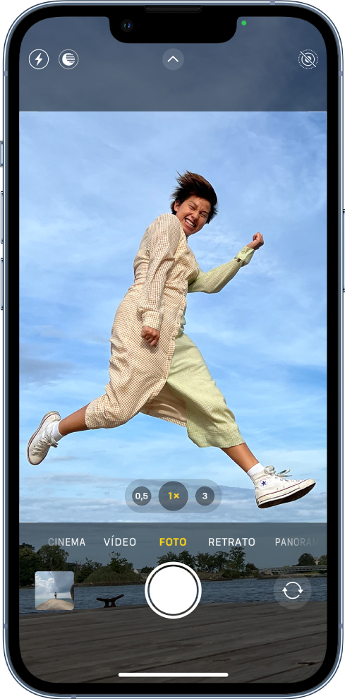 Tela da Câmera no modo Foto, com outros modos à esquerda e à direita, abaixo do visor. Os botões do Flash, modo Noite, Controles da Câmera e Live Photo aparecem na parte superior da tela. Abaixo dos modos da câmera, da esquerda para a direita, o botão Visualizador de Fotos e Vídeos, o botão Tirar Foto e o botão Seletor de Câmera Traseira.