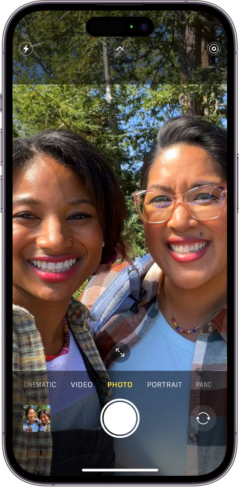 Ekrani për Camera në modalitetin Photo. Nën modalitetet e kamerës janë, nga e majta dhe të djathtë, butoni Photo and Video Viewer, butoni Take Picture dhe butoni Camera Chooser Back-Facing. Butonat për Flash, Camera Controls dhe Live Photo ndodhen në krye të ekranit. Brenda kuadrit të kamerës, subjektet janë duke nxjerrë selfi.