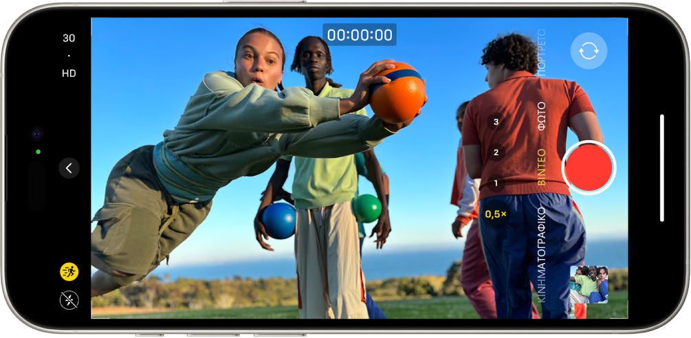 Το iPhone περιστρέφεται σε οριζόντιο προσανατολισμό. Η Κάμερα είναι ανοιχτή στη λειτουργία Βίντεο. Κουμπιά για το φλας και τη λειτουργία Δράσης εμφανίζονται στην κάτω αριστερή γωνία της οθόνης και η λειτουργία Δράσης είναι ενεργοποιημένη. Το κουμπί «Στοιχεία ελέγχου Κάμερας» βρίσκεται στο αριστερό κέντρο της οθόνης, και στην πάνω αριστερή γωνία υπάρχουν γρήγοροι διακόπτες για εναλλαγή της ανάλυσης βίντεο και του ρυθμού καρέ. Στη δεξιά πλευρά βρίσκονται, από πάνω προς τα κάτω, το κουμπί «Επιλογέας πίσω κάμερας», το κουμπί «Εγγραφή» και το κουμπί «Προβολή φωτογραφιών και βίντεο». Μέσα στο πλαίσιο της κάμερας, εμφανίζεται ένα άτομο που τρέχει.