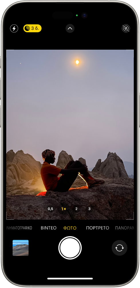 Η οθόνη της Κάμερας στη λειτουργία «Φωτογραφία». Κουμπιά για το φλας και τη Νυχτερινή λειτουργία εμφανίζονται στην πάνω αριστερή γωνία της οθόνης και η Νυχτερινή λειτουργία είναι ενεργοποιημένη. Το κουμπί «Στοιχεία ελέγχου κάμερας» βρίσκεται πάνω στο κέντρο και το κουμπί Live Photo βρίσκεται στην πάνω δεξιά γωνία. Στο κάτω μέρος της οθόνης βρίσκονται, από αριστερά προς δεξιά, το κουμπί Προβολής φωτογραφιών και βίντεο, το κουμπί Λήψης φωτογραφίας, και το κουμπί Επιλογέα πίσω κάμερας. Μέσα στο πλαίσιο της κάμερας, υπάρχει μια νυχτερινή σκηνή.