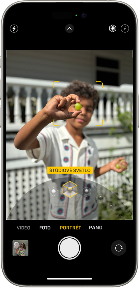 Obrazovka Kamera v režime Portrét. Objekt v hľadáčiku je zaostrený, pozadie naopak rozostrené. V dolnej časti rámčeka je otvorený kruhový ovládač na výber osvetlenia portrétu a na ňom je vybraný efekt Štúdiové svetlo. V ľavom hornom rohu obrazovky je tlačidlo Blesk, v strede hornej časti je tlačidlo Ovládanie kamery a vpravo hore sú tlačidlá na úpravu intenzity osvetlenia portrétu a hĺbky ostrosti. V spodnej časti obrazovky sú sprava doľava nasledovné tlačidlá: tlačidlo prehliadača fotiek a videí, tlačidlo Odfotiť a tlačidlo na výber kamery prepnuté na zadnú kameru