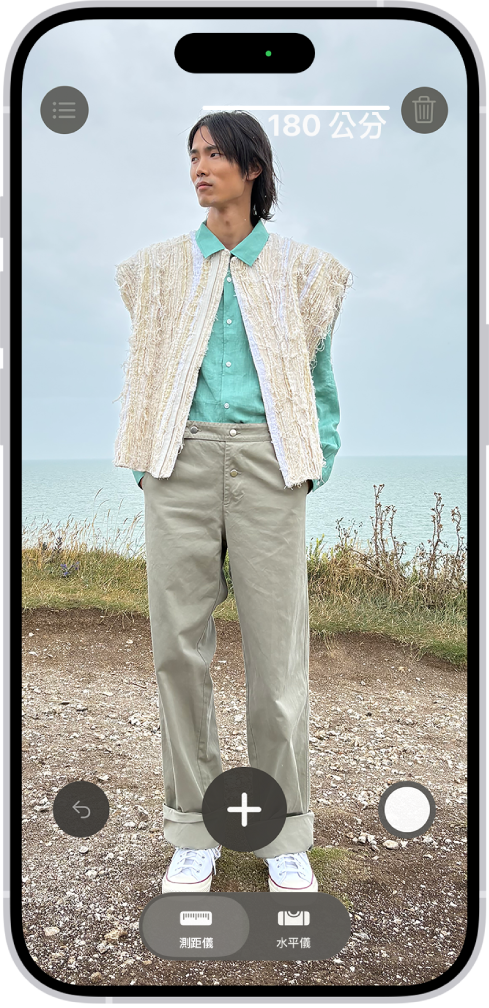 在「測距儀」App 中測量一個人的身高,身高測量結果顯示在此人頭頂上方。畫面右下角附近有可用來拍下量測結果的「拍照」按鈕。畫面頂部顯示綠色的「相機使用中」指示器。