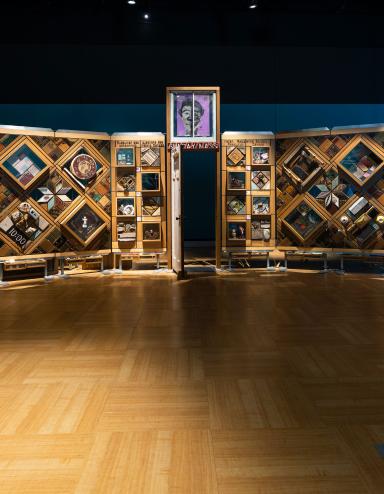 An interconnected series of panels made of cedar wood that stand together like a bunch of walls with various objects on them. Partially obscured.