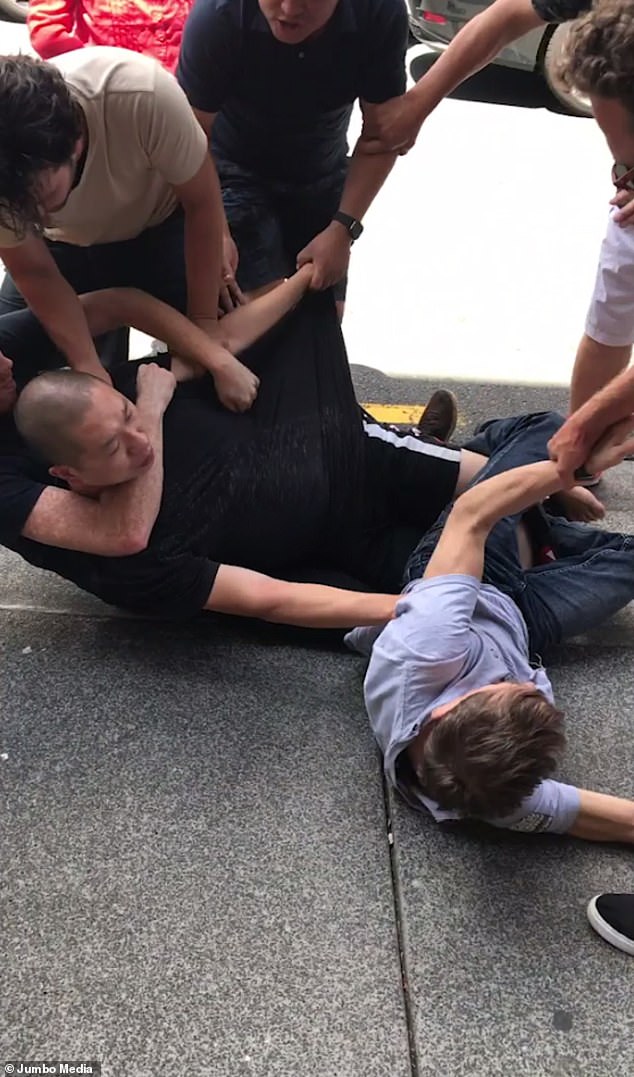 Two men fell to the pavement before another five people join in on the melee . One pulled the man in the black shirt away with their arm around his neck