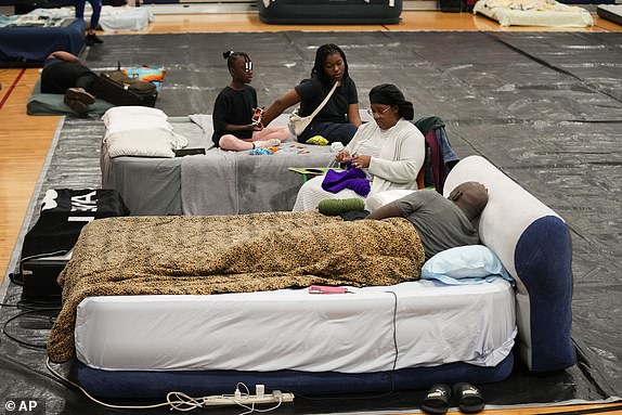 Sharonda and Victor Davis, of Tallahassee, sit with their children Victoria background left, and Amaya, background right, inside a hurricane evacuation shelter at Fairview Middle School, ahead of Hurricane Helene, expected to make landfall here today, in Leon County, Fla., Thursday, Sept. 26, 2024. (AP Photo/Gerald Herbert)