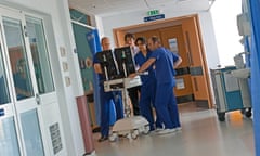 Surgical staff in wearing dark blue scrubs stand looking at scans on a screen in a hospital corridor