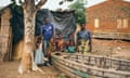 A family – two adults and five young children – stand by a tree with a shack behind them