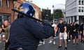 Helmeted police officer with a baton over their right shoulder faces protesters in a Bristol street.