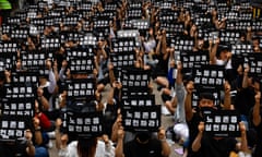 Neat rows of adults sitting cross-legged hold up identical black signs with white Korean type on it.