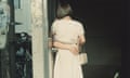 Untitled, 1996, by Hara Mikiko shows the back of a woman in a doorway, holding a handbag, in an embrace with a figure whose arm is the only thing visible.