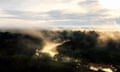 Mist above dense rainforest at dawn with the rising sun glinting on a river