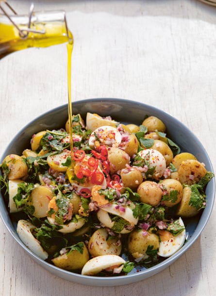 Olive oil being poured onto a bowl of potatoes with green and red garnish