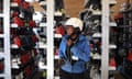 A skier smiles while holding her ski helmet strap amid shelves of boots