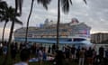 A vast modern multi-deck cruise liner sailing close to shore. dwarfing the large crowd who have come to look at it