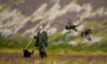 A gamekeeper, with a black dog, stands among heather in the background as two grouse fly across the landscape in front