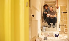 Young couple sitting on the dust sheets on the stairs and looking through the paint sample cards