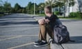 Lonely teenage boy sitting on a kerb next to a  school.