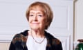 Margaret Hodge, in a cardigan, smiles as she sits on a desk in her Portcullis House office between two table lamps