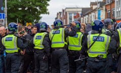 A line of police in riot gear face a crowd of people in a road