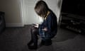 A young girl in school uniform sat on a stool in the middle of a room using a mobile phone.