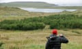 Jon Macleod in red beanie looking out at loch with garden fork over his shoulder