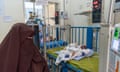 A woman in a niqab looks at a small baby lying in a cot and hooked up to machines in a hospital