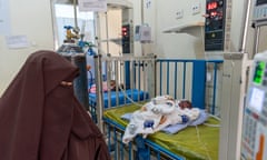 A woman in a niqab looks at a small baby lying in a cot and hooked up to machines in a hospital