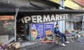 A man sits on a chair outside a destroyed convenience store