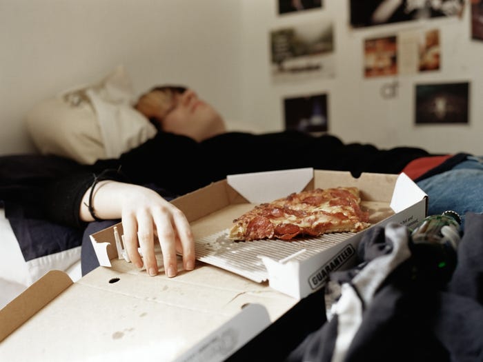 a teen boy in bed with his hand in a pizza box