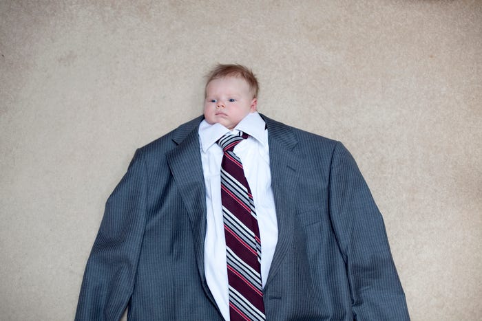 A baby lays on the floor, dressed in a full-sized pin-stripe suit.