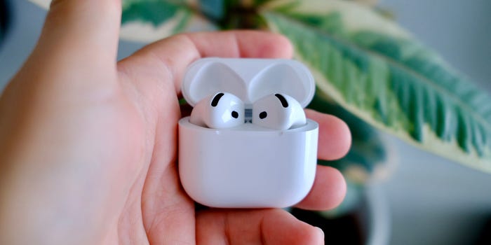 Apple AirPods 4 in their case being held in hand in front of a plant.