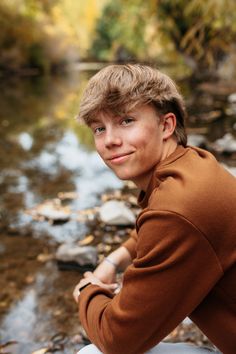 a young man sitting on top of a rock next to a river