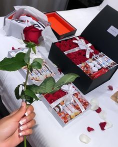 a person is holding a rose in front of two boxes of chocolates and roses