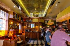 people sitting at tables in a restaurant with checkered flooring and yellow lights hanging from the ceiling