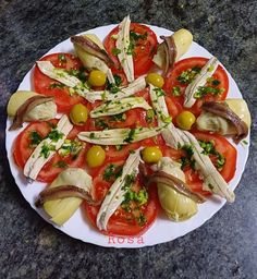 a white plate topped with sliced tomatoes and olives