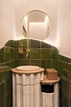 a bathroom with green and white tiles on the walls, sink and mirror above it